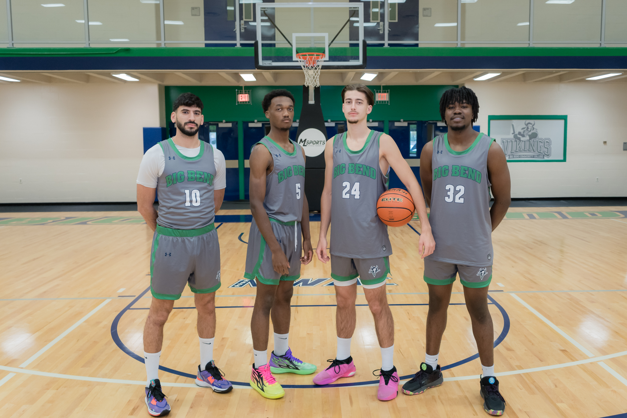 four basketball players posing together in front of the hoop