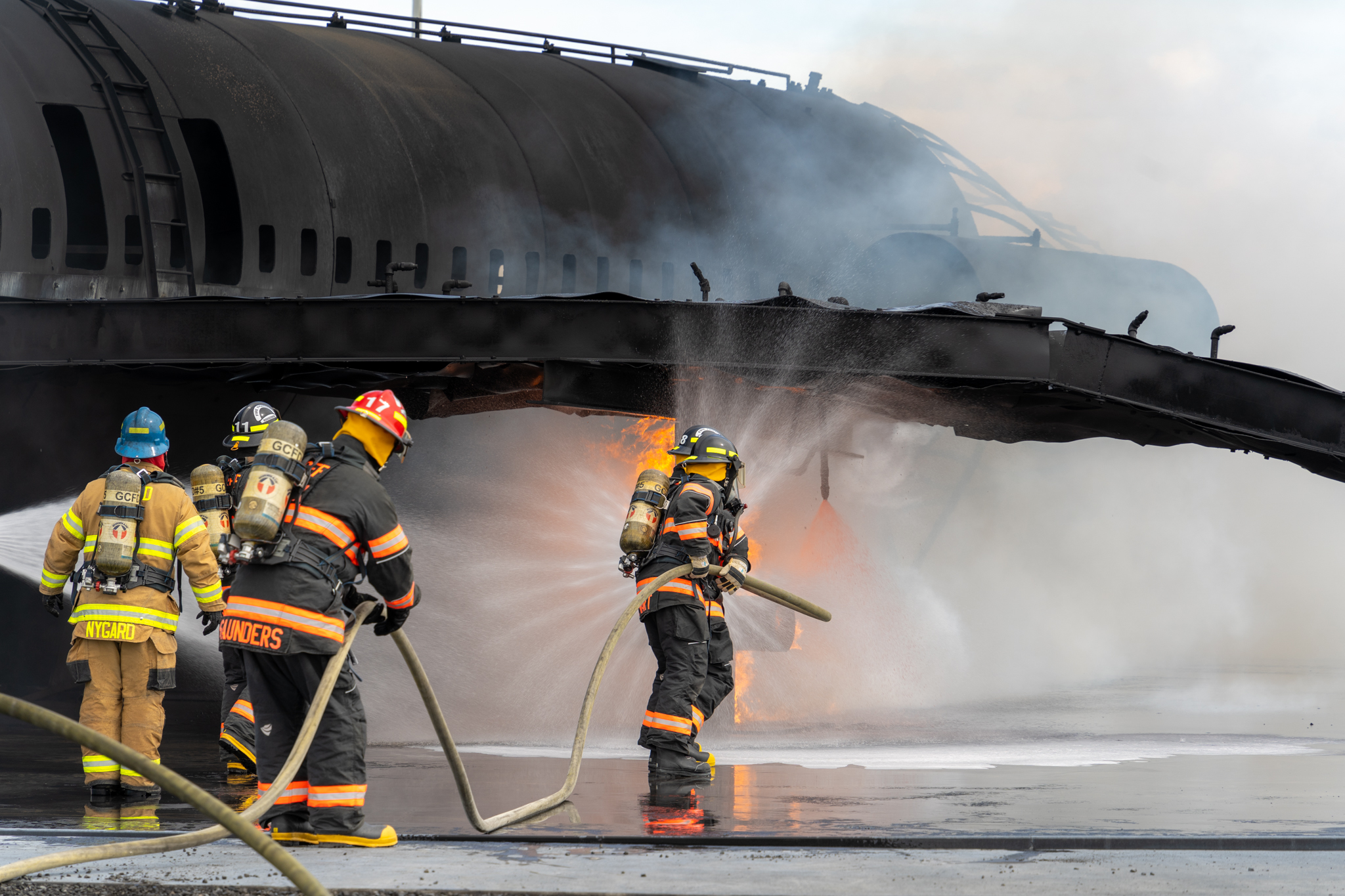 Four firefighters spraying water on burning plane from a different angle